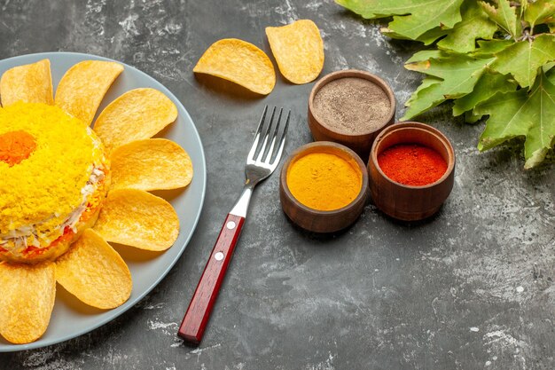 Zijaanzicht van de salade aan de linkerkant met kruidenvorkchips en bladeren aan de zijkant op donkergrijze tafel