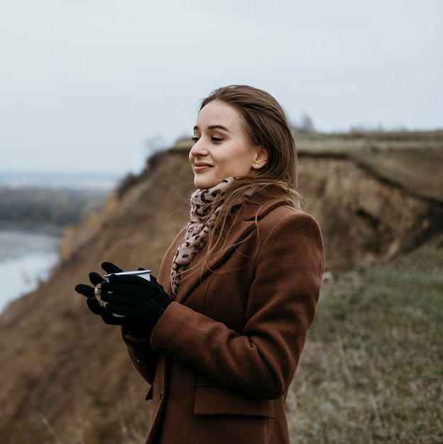 Zijaanzicht van de vrouw die het meer bewondert met terwijl hij warme drank vasthoudt