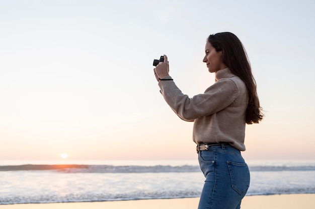 Gratis foto zijaanzicht van de vrouw die het strand met exemplaarruimte fotografeert