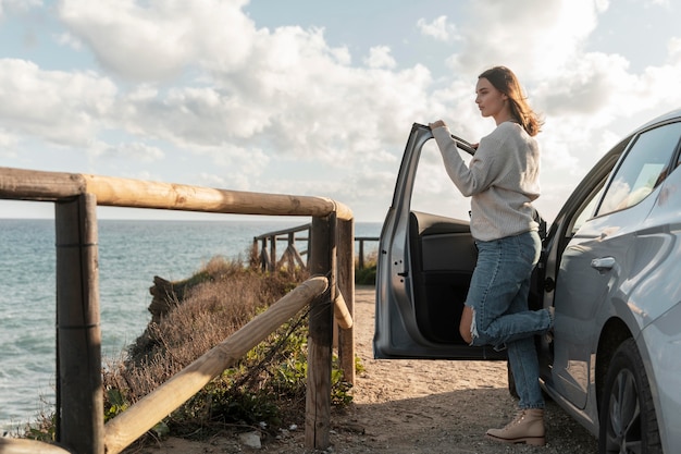 Gratis foto zijaanzicht van de vrouw die het uitzicht op het strand vanuit haar auto bewondert