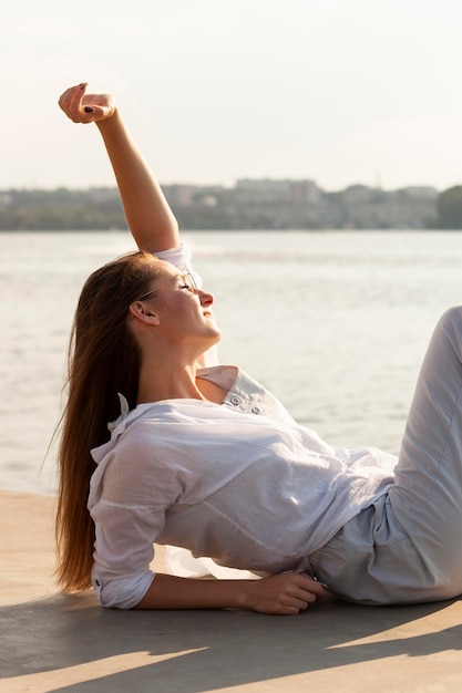 Zijaanzicht van de vrouw die van de zon naast het meer geniet