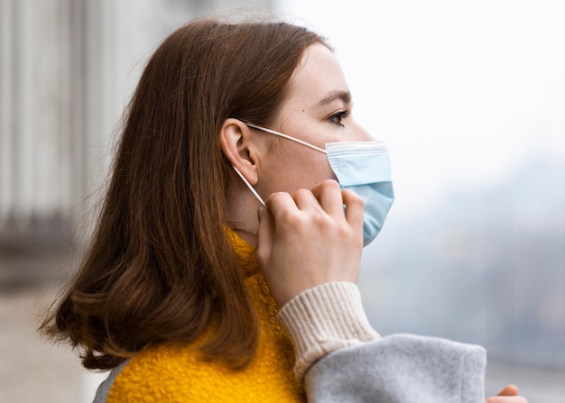 Zijaanzicht van de vrouw in de stad die haar medisch masker aanpast