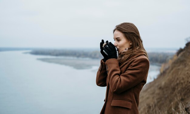 Zijaanzicht van de vrouw met een warme drank aan het meer