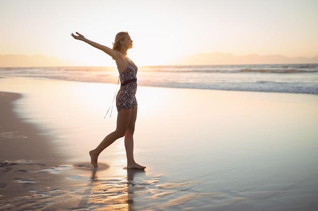 Zijaanzicht van de vrouw met uitgestrekte armen staande op het strand