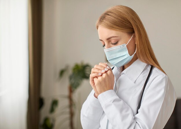 Zijaanzicht van de vrouwelijke arts van het covid-herstelcentrum met een stethoscoop en het medische masker bidden