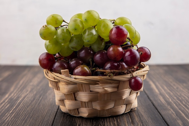 Zijaanzicht van druiven in mand op houten oppervlak en witte achtergrond