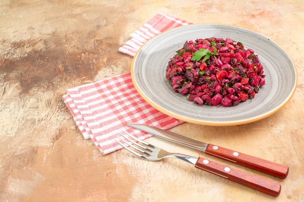 Zijaanzicht van een bord met een rode salade met groenten erop met een ingecheckt servet en de vork en het mes aan de zijkant op een houten backgorund