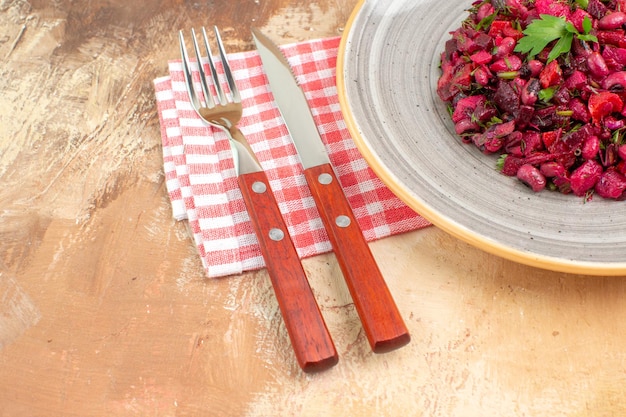 Zijaanzicht van een bord met een rode salade met groenten erop met een ingecheckt servet en het bestek aan de zijkant op een houten backgorund