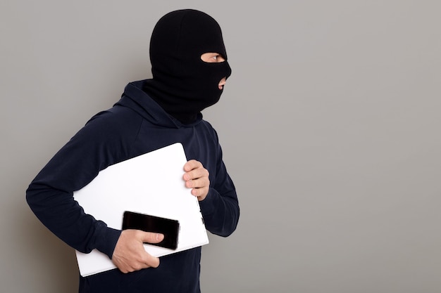 Gratis foto zijaanzicht van een criminele man die met een gestolen laptop ontsnapt