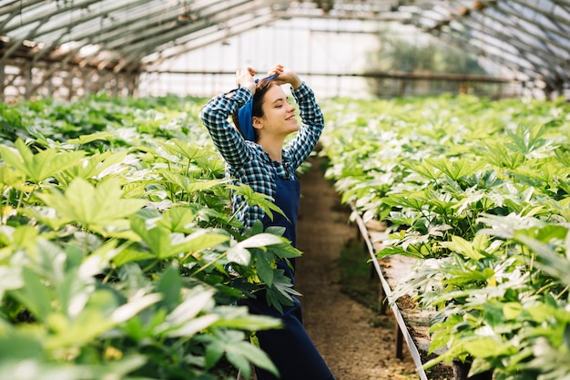 Gratis foto zijaanzicht van een gelukkige vrouwelijke tuinman die zich in serre bevindt