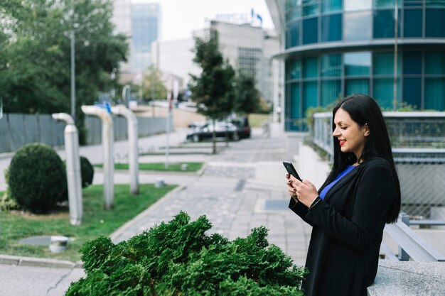 Zijaanzicht van een glimlachende onderneemster die mobiele telefoon met behulp van