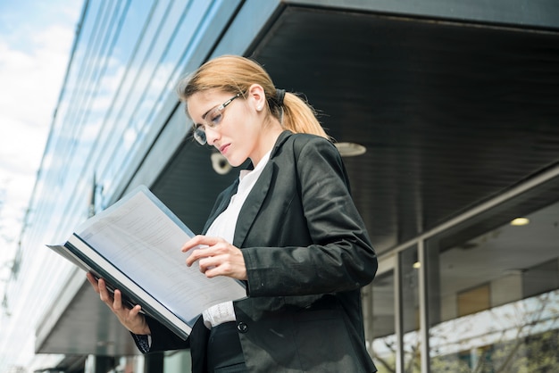 Zijaanzicht van een jonge onderneemster die zich onder het collectieve gebouw bevindt dat het document leest