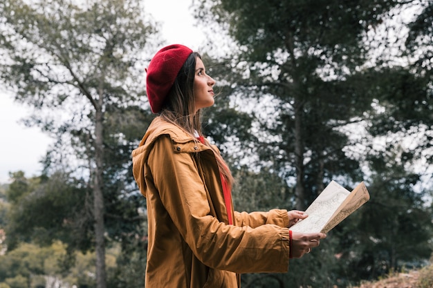 Gratis foto zijaanzicht van een jonge vrouw die de kaart houdt die in het bos zich bevindt