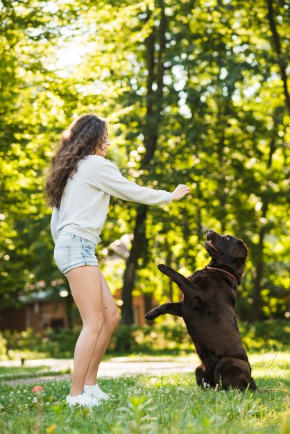 Zijaanzicht van een jonge vrouw die pret met haar hond in tuin heeft