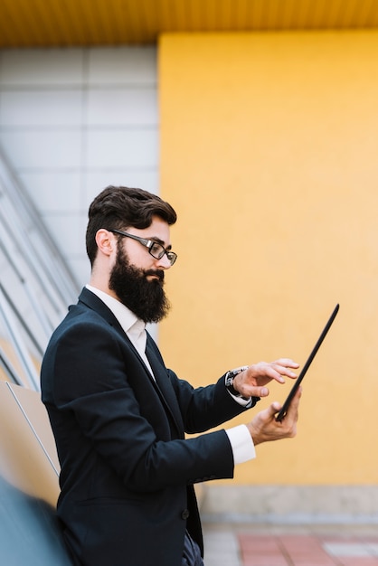 Zijaanzicht van een jonge zakenman die digitale tablet gebruiken die zich tegen muur bevinden