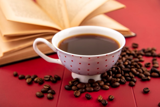 Zijaanzicht van een kopje koffie met koffiebonen geïsoleerd op een rode achtergrond