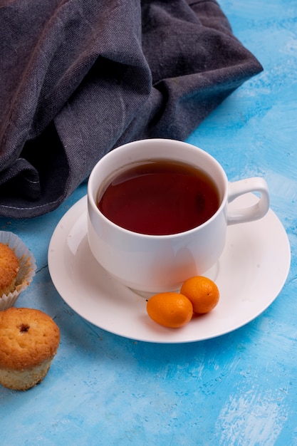 Gratis foto zijaanzicht van een kopje thee met smakelijke muffin op blauwe tafel