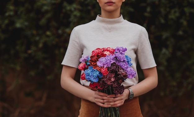 Zijaanzicht van een meisje met een multi-clored boeket van anjerbloemen op donkere muur