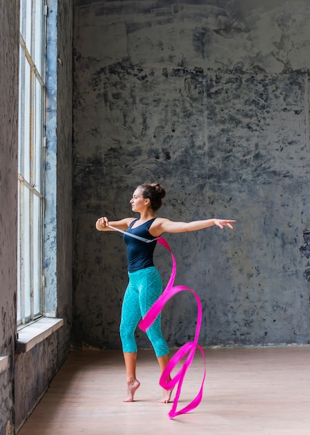 Gratis foto zijaanzicht van een mooie jonge vrouw die met roze lint danst