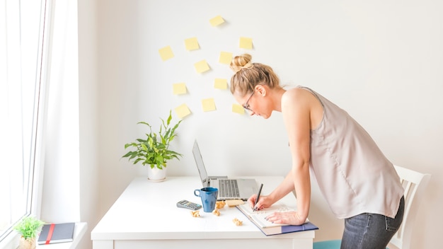 Gratis foto zijaanzicht van een onderneemster het schrijven programma in agenda op het werk