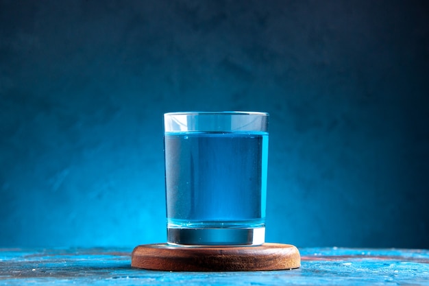 Zijaanzicht van een stilstaand water in een glas op houten snijplank op blauwe achtergrond