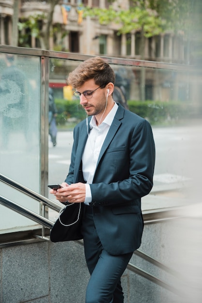 Gratis foto zijaanzicht van een zakenman die mobiele telefoon met zijn oortelefoon in oren met behulp van