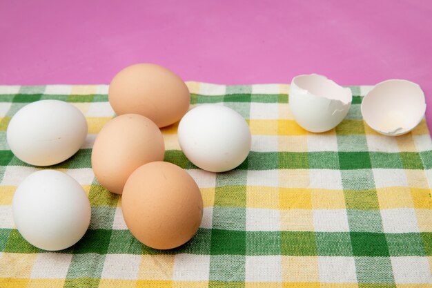 Zijaanzicht van eieren met eierschaal op doek oppervlak en paarse achtergrond