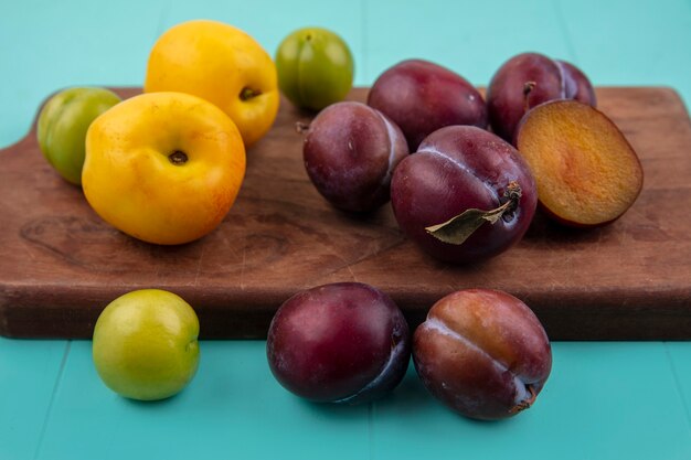 Zijaanzicht van fruit als nectacots, pruimen en plukken op snijplank en op blauwe achtergrond