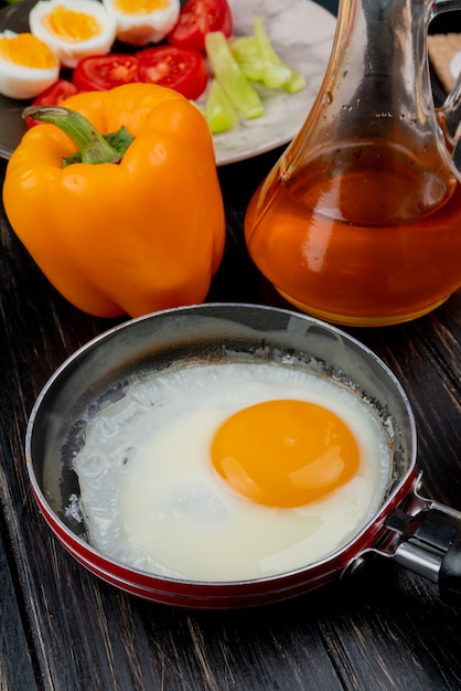 Zijaanzicht van gebakken ei op een koekenpan met appelazijn met een oranje peper op een houten achtergrond