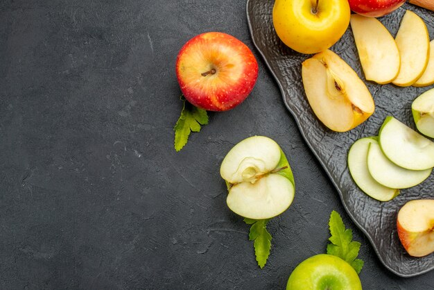 Zijaanzicht van groengele en rode gesneden en hele verse appels op een zwart dienblad en kaneellimoenen op een donkere tafel