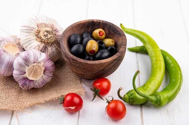 Zijaanzicht van groenten als knoflookbollen op zak en kom met olijven met paprika en tomaten op hout