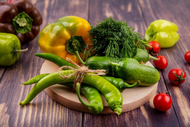 Zijaanzicht van groenten als peper, komkommer dille op snijplank met tomaten op hout