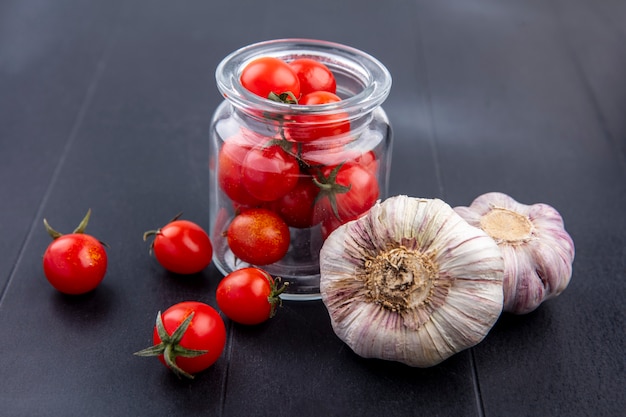 Gratis foto zijaanzicht van groenten als tomaten in glazen pot en knoflookbollen op zwart