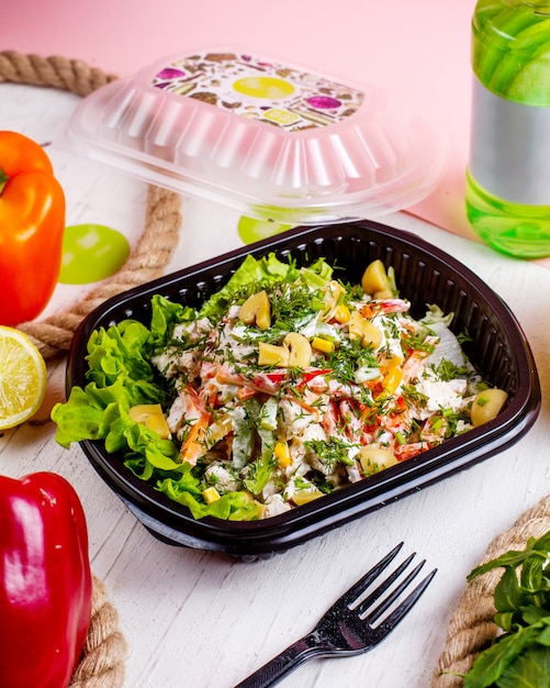 Zijaanzicht van groentesalade met de worteldille van paddestoelengroene paprika's en roomsaus in leveringsdoos