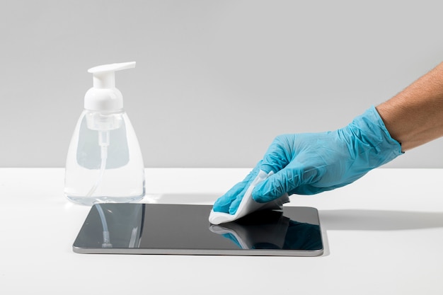 Gratis foto zijaanzicht van hand met chirurgische handschoen desinfecterende tablet op bureau