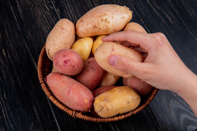 Zijaanzicht van hand met potatowith mand vol aardappelen op houten tafel