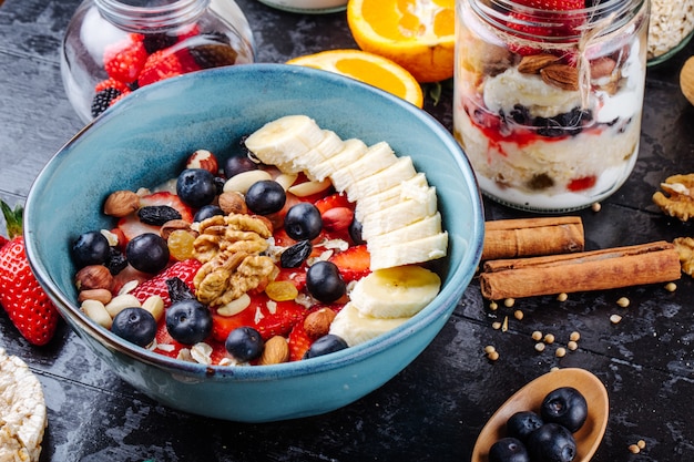 Zijaanzicht van havermoutpap met aardbeien, bosbessen, bananen, gedroogd fruit en noten in een keramische kom op tafel