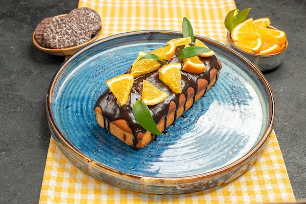 Zijaanzicht van heerlijke cake versierd op geel gestreepte handdoek en koekjes op zwarte tafel