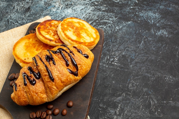 Zijaanzicht van heerlijke croissantpannenkoeken op houten snijplank voor geliefde aan de rechterkant op donkere ondergrond