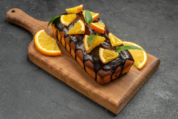 Zijaanzicht van heerlijke taarten versierd met orangen en chocolade op snijplank op zwarte tafel