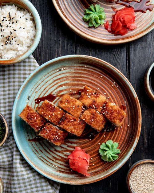 zijaanzicht van hete gebakken sushi rolt met zalm avocado en kaas geserveerd met gember en wasabi op een bord op houten tafel