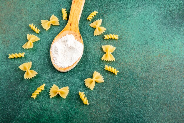 Zijaanzicht van houten lepel met bloem met rauwe pasta op een groen oppervlak