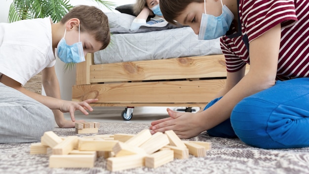 Zijaanzicht van jonge geitjes die jenga thuis spelen terwijl het dragen van medische maskers