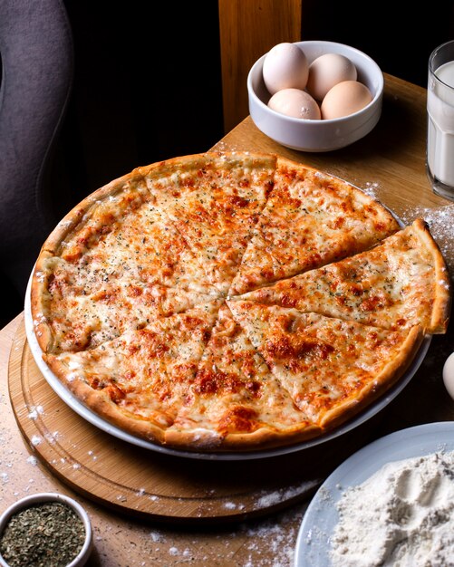 Zijaanzicht van kaas pizza met tomaten en kruiden op houten tafel