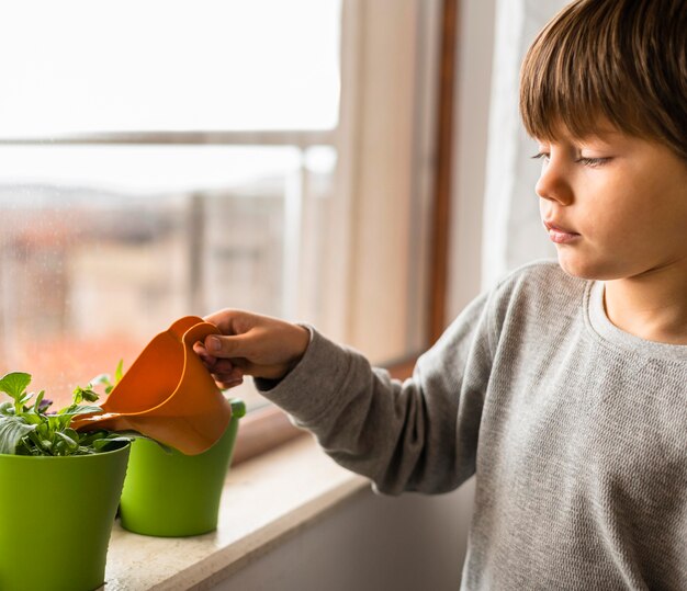 Zijaanzicht van kind planten water geven bij het raam