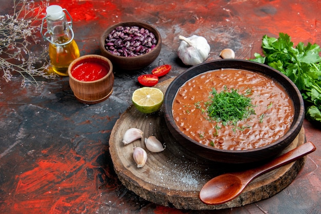 Zijaanzicht van klassieke tomatenzeep bonen knoflook lepel olie fles citroenketchup op gemengde kleurentafel