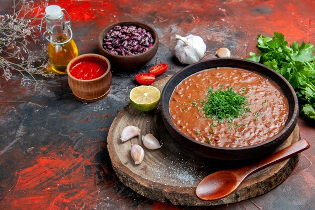 Zijaanzicht van klassieke tomatenzeep bonen knoflook lepel olie fles citroenketchup op gemengde kleurentafel