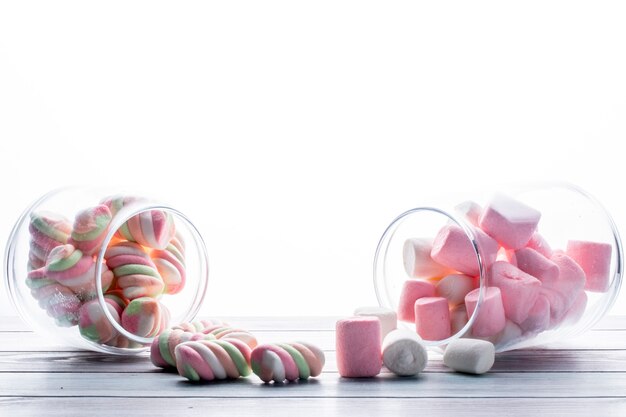 Zijaanzicht van kleurrijke gedraaide marshmallow verspreid uit een glazen pot op wit