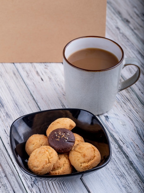 Zijaanzicht van koekjes in een zwarte kom en een kop met cacao op houten