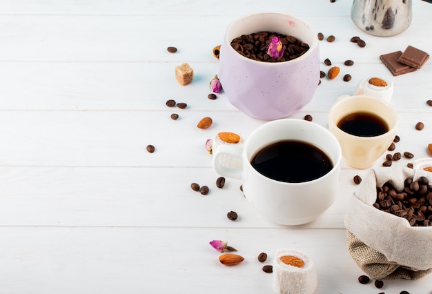 Zijaanzicht van koffiebonen in een kom en kopjes koffie op witte achtergrond met kopie ruimte